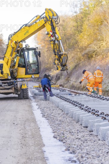 Excavators and workers lay rail blocks on a construction site on an autumn day, track construction