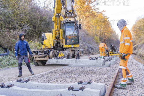 Workers lay concrete blocks for rails with an excavator on a construction site, track construction