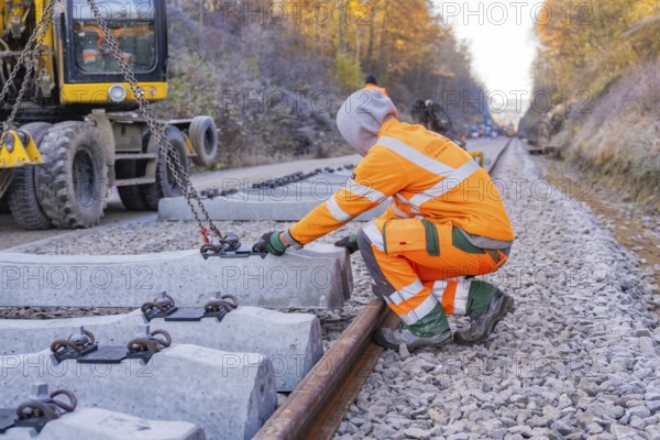 A construction worker wearing glowing safety clothing works on sleepers along the railway line,