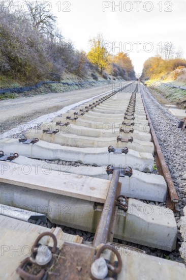 Behind a railroad, a long, straight section of track stretches through autumnal nature, track