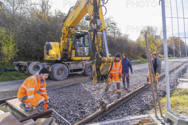 Construction workers in orange clothing work next to a yellow excavator on a railway line, track