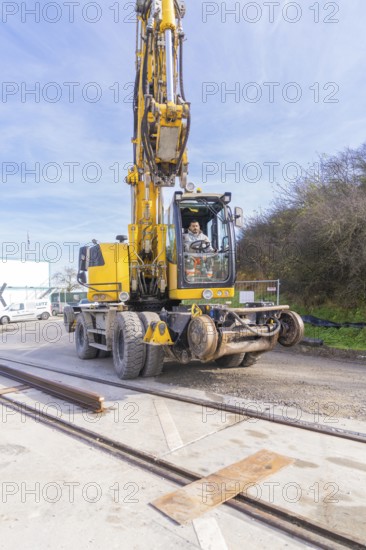 A yellow excavator on a construction site with tracks in the foreground. The sky is clear and the