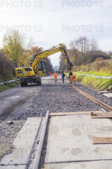 Construction workers lay tracks on a construction site while a yellow excavator assists. Autumn