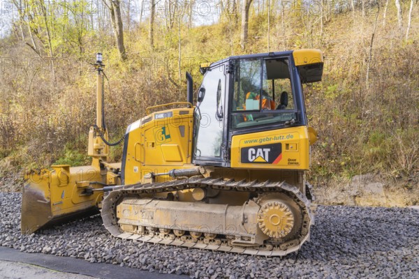 CAT chain tractor on gravel, autumn vegetation during construction work in the background, Hermann