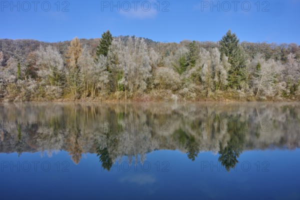 A quiet autumn picture with a lake whose water reflects an autumnal forest, hoarfrost, winter,