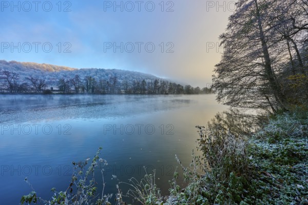 A frosty morning on the river with trees and reflecting water in shades of blue and gold,