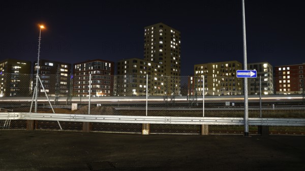 One way street on the fence, behind it a passing ICE train, illuminated apartments in a new housing