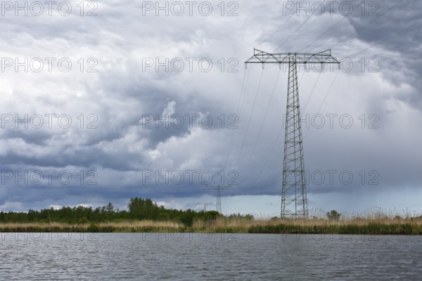 Landscape with high power pole under dramatic waterside cloud formations, Peenetal nature park