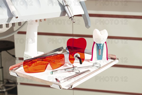On the tray are various dental instruments, a model dental implant and bright orange safety