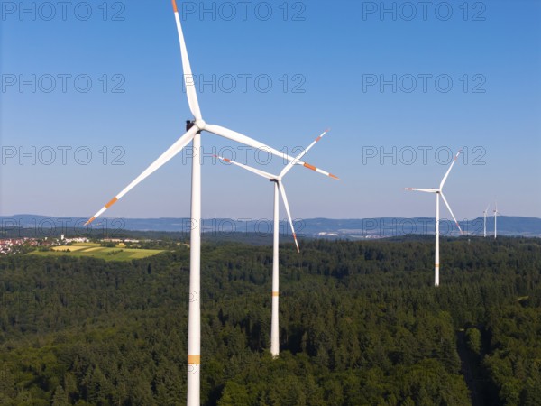 Three wind turbines rise above a green forest under a clear sky, near Schorndorf, Remstal,
