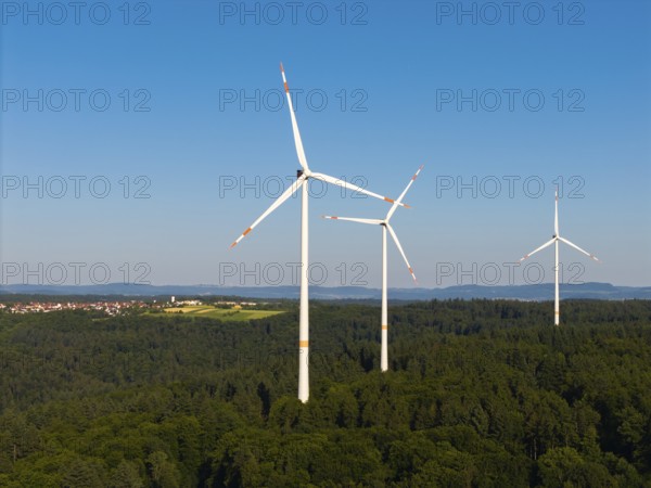 Three wind turbines above a dense forest area under a clear sky, near Schorndorf, Remstal,