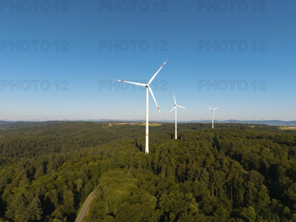 A series of wind turbines on a wooded hill under a wide blue sky, near Schorndorf, Remstal,