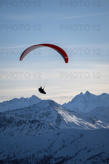 Paragliders flying over snowy mountain peaks in winter in evening light, Kitzbühel Alps, Tyrol,
