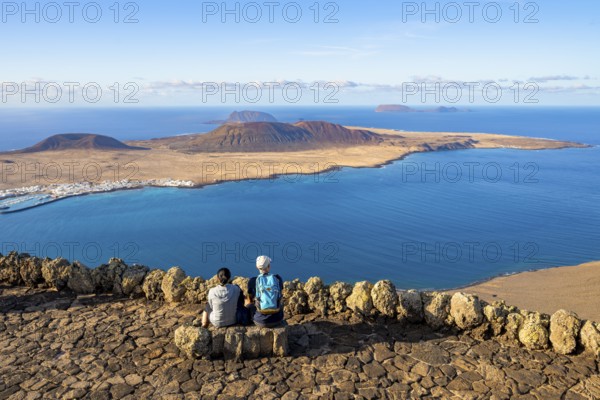 Tourists on a bench on the viewing platform at the Mirador del Río viewpoint, in the evening light,