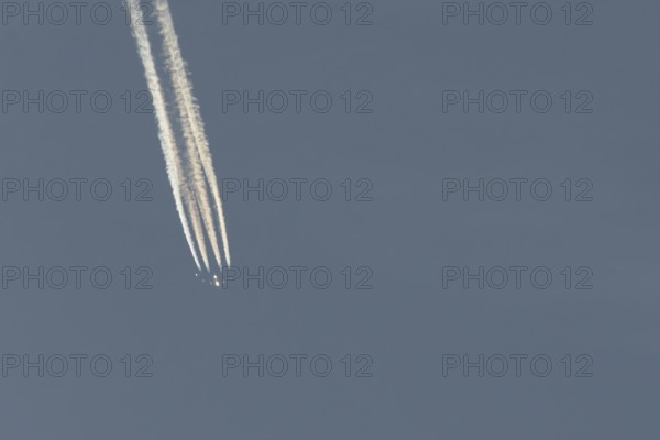 Jet passenger aircraft flying in a blue sky with contrails or vapour trails behind, England, United