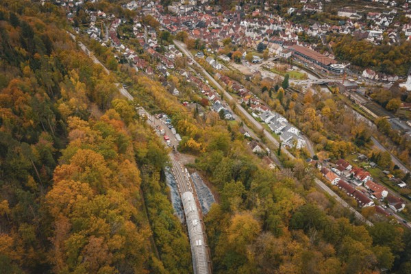 Aerial view of a city next to an autumnal forest landscape with train tunnel, Hermann-Hesse-Bahn