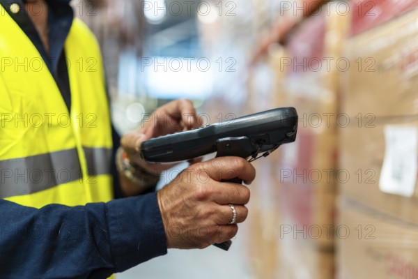 Warehouse worker in high visibility vest and blue uniform scanning barcodes on boxes with handheld