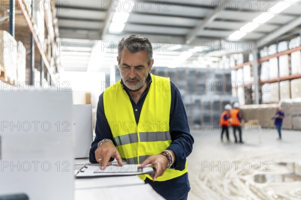Experienced manager wearing a high visibility safety vest confirming details on a clipboard while