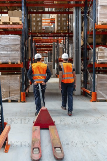 Warehouse workers in safety vests and hard hats navigating through industrial shelving with a