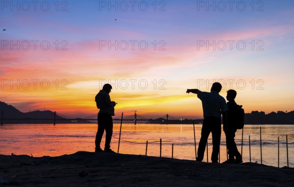 People enjoy the vibrant sunset by the Brahmaputra riverside, capturing photos and moments against