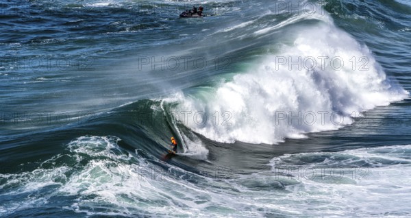 Surfers with their jet ski pilots in the Atlantic waves below Farol de Nazaré, Forte São Miguel,