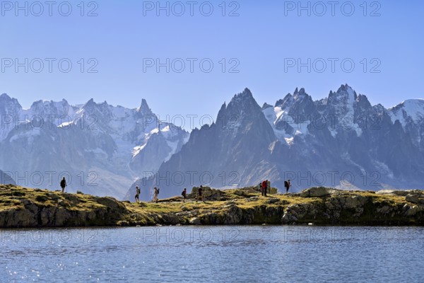 A group of hikers at Lac de Chésserys, behind the snow-covered Mont Blanc massif,