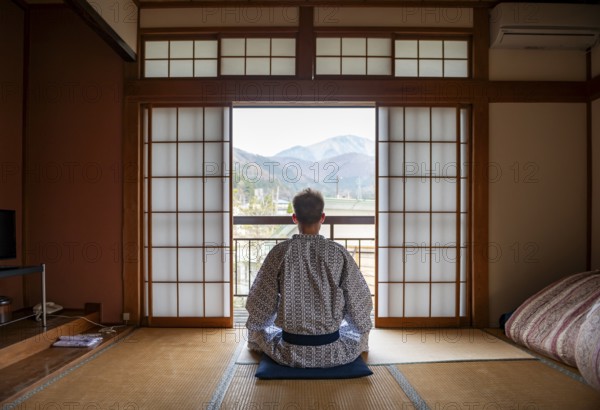 Young man wearing kimono sitting in traditional Japanese living room with tatami mats and shoji