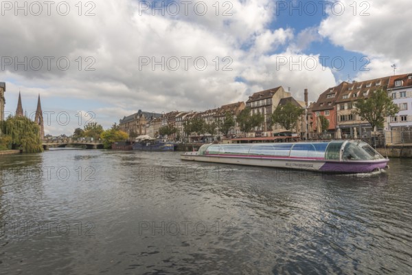 A pleasure boat glides peacefully on the Strasbourg River. Colourful buildings and trees line the