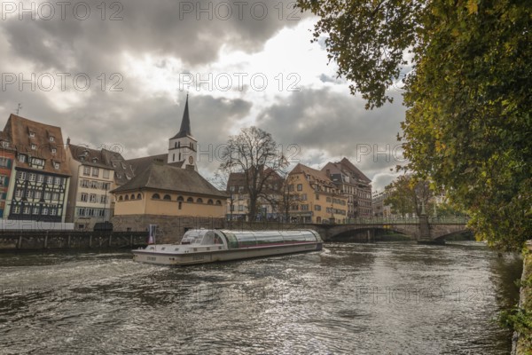 Boat sails gently on river in Strasbourg. Historic houses are located on the banks. The sky is