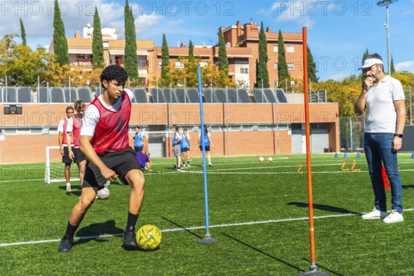 Young male student athlete concentrating on dribbling a soccer ball between poles during a drills