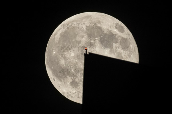 The full moon sweeps along the Frankfurt evening sky and passes the tip of the European Central