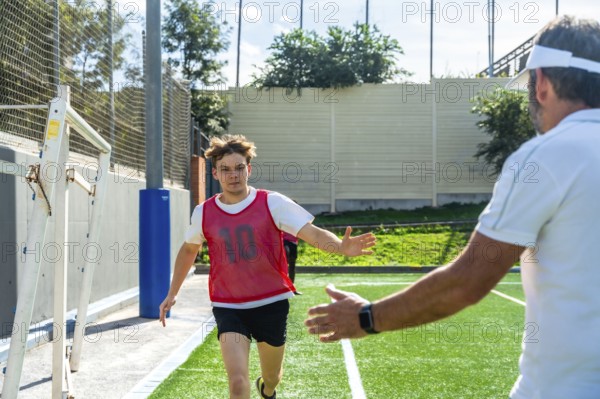 Youth male soccer player in a red bib running towards a coach with outstretched arms, receiving