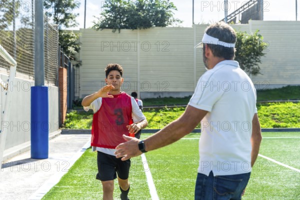 Youth male soccer player in a red bib running towards a male coach with an outstretched hand,