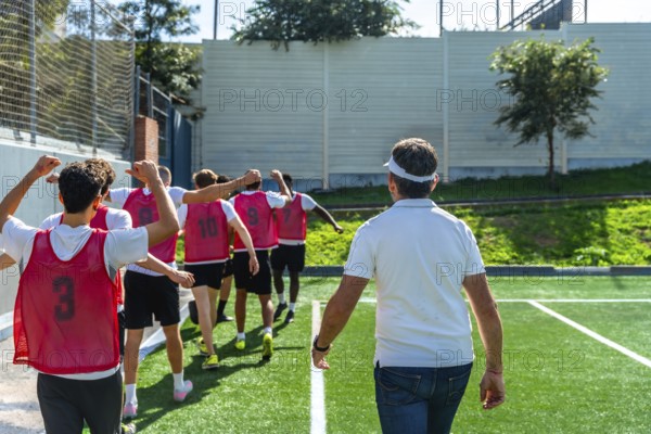 Youth soccer coach leading a group of players in red training vests across artificial grass,