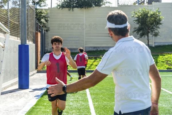 Soccer coach extending hand for a high five with a young male player wearing a red bib during a