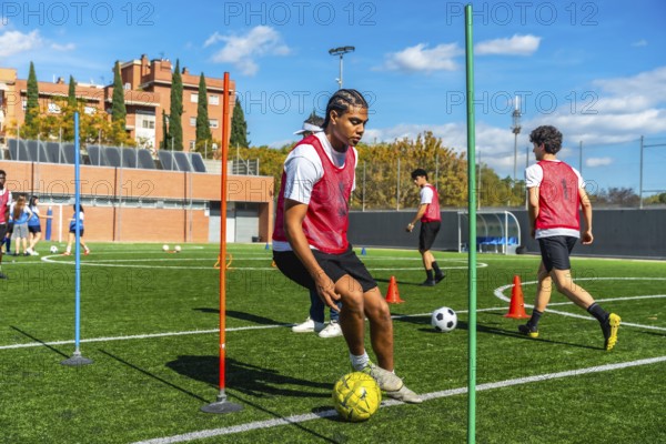 Young man in a red vest training soccer dribbling techniques on a green artificial turf field,