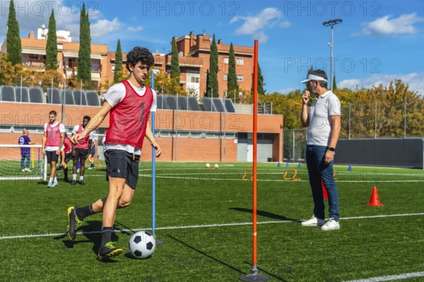 Soccer player training during an agility drill on a green field, dribbling a ball around poles