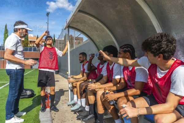 Soccer coach briefing male players on the sideline bench during a break, discussing strategy and