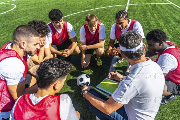 Soccer coach providing strategic instructions to his diverse team of young male players, gathered