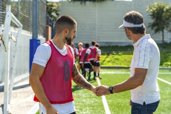 Coach and young soccer player shaking hands on a green sports field, demonstrating teamwork,