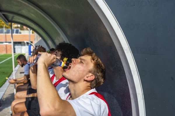 Soccer teammates on the bench rehydrating with bottled water during a break in training or a match,