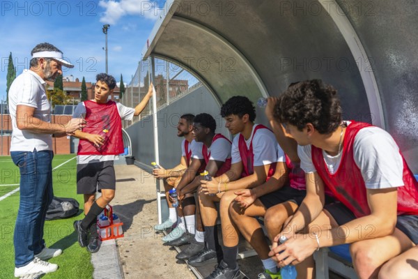 Soccer coach talking and giving instructions to his diverse team of young male athletes sitting on