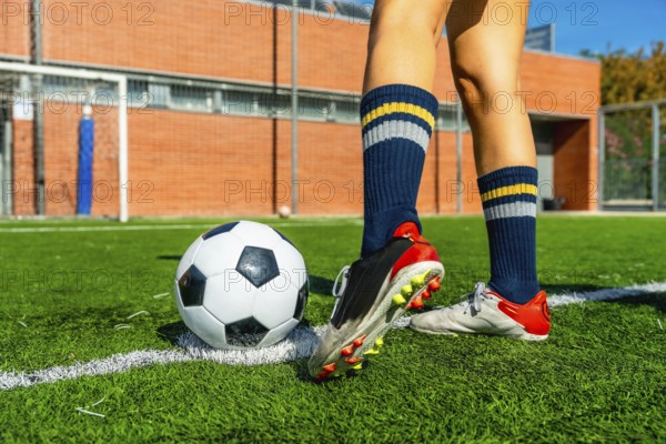 Female soccer player's legs and feet are positioned near a soccer ball on a green artificial turf
