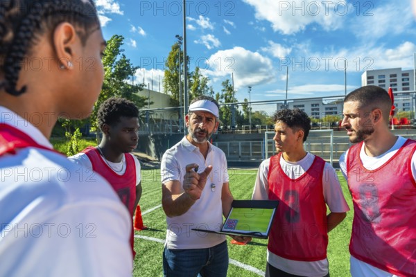 Soccer coach explaining game strategy to a diverse group of male players on a green artificial turf