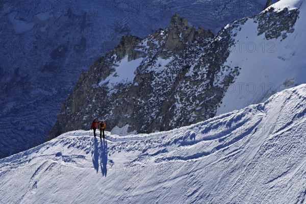 Two ascended mountaineers run across a snow-covered mountain ridge, Aiguille du Midi,
