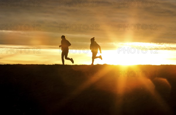Woman and child walk across a dike on the island of Fehmarn at sunset, 13.10.2025, Fehmarn,