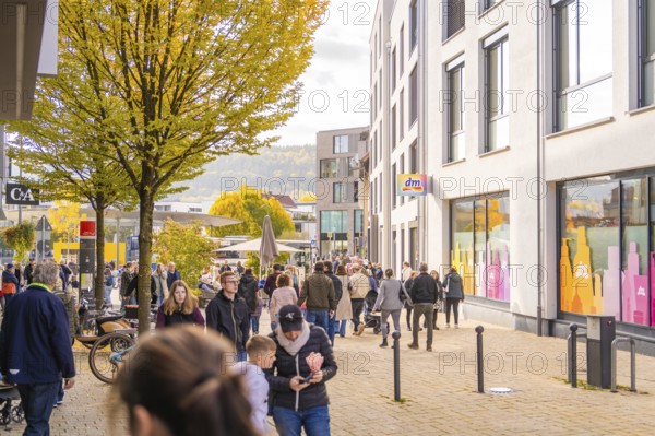 Busy shopping street in autumn, people strolling between modern buildings and colorful shops,