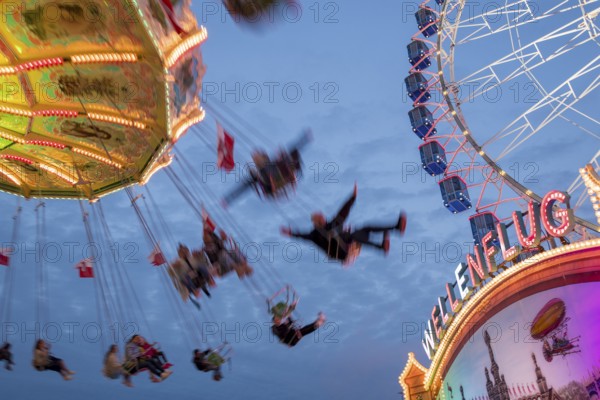 An illuminated chain carousel turns at night at a funfair, with floating people and colourful