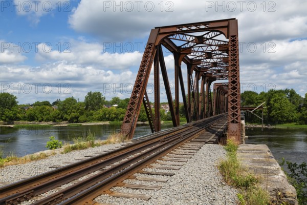 Railroad tracks leading to old rusted Terrebonne Pratt truss railroad bridge over Des Mille-Iles