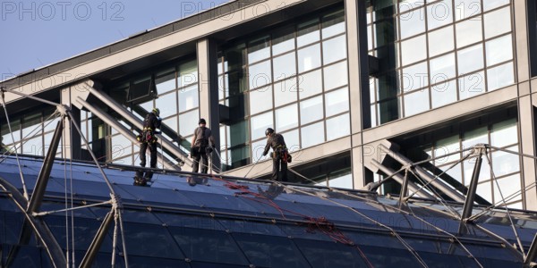 Three male glass cleaners abseiling down a glass roof of Berlin Central Station to clean windows,